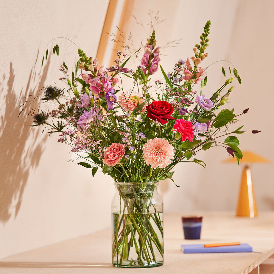 Sfeerfoto van een boeket bloemen in een vaas. Het boeket bloemen bevat o.a. bont en pastelgekleurde gerbera’s, leeuwenbekjes en rozen.